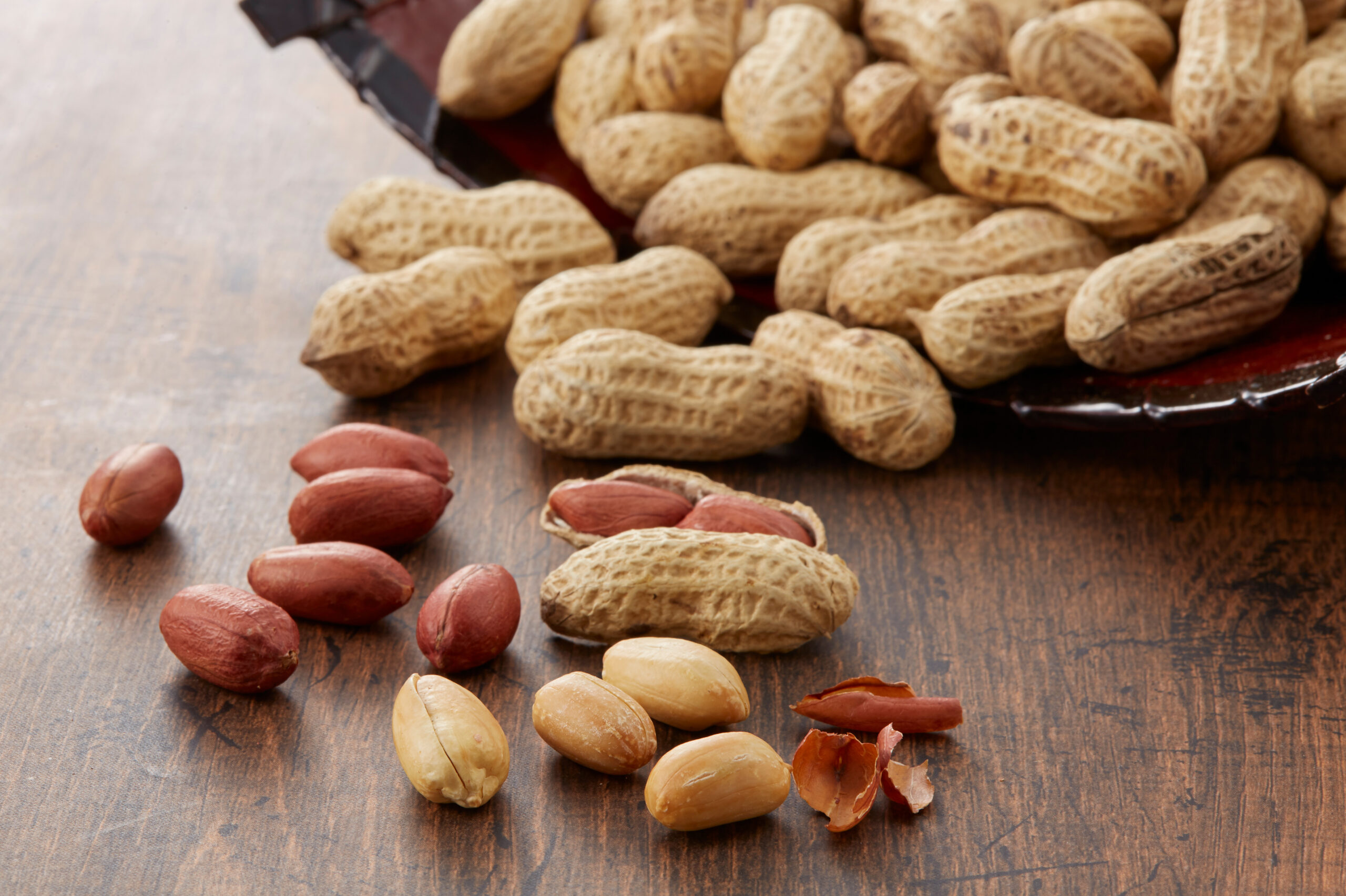 Peanuts in shells and several shelled peanuts scattered on a wooden surface.